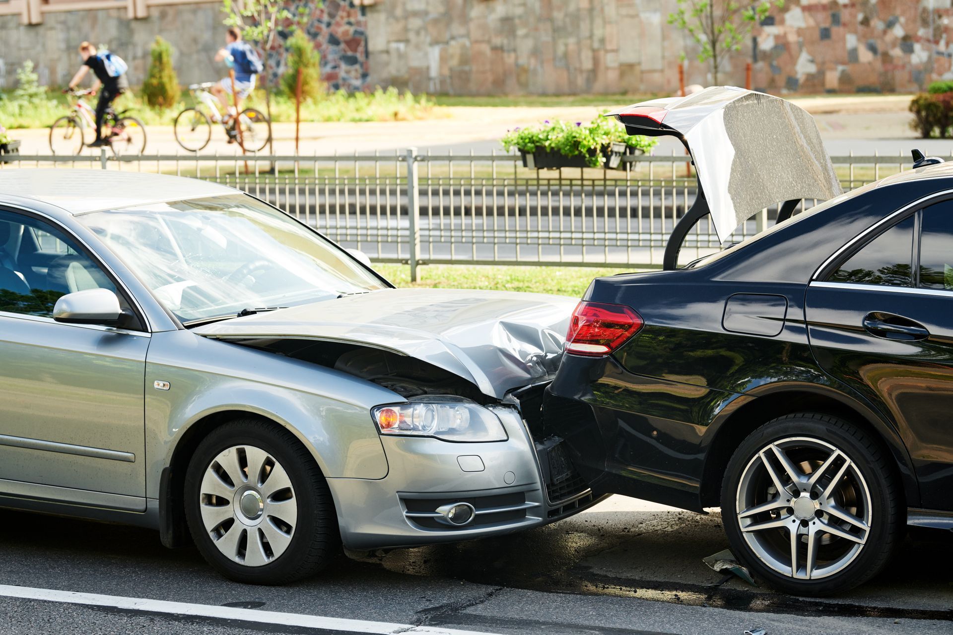 Two cars damaged in a collision on a city street. Silver car front damaged; black car rear damaged.