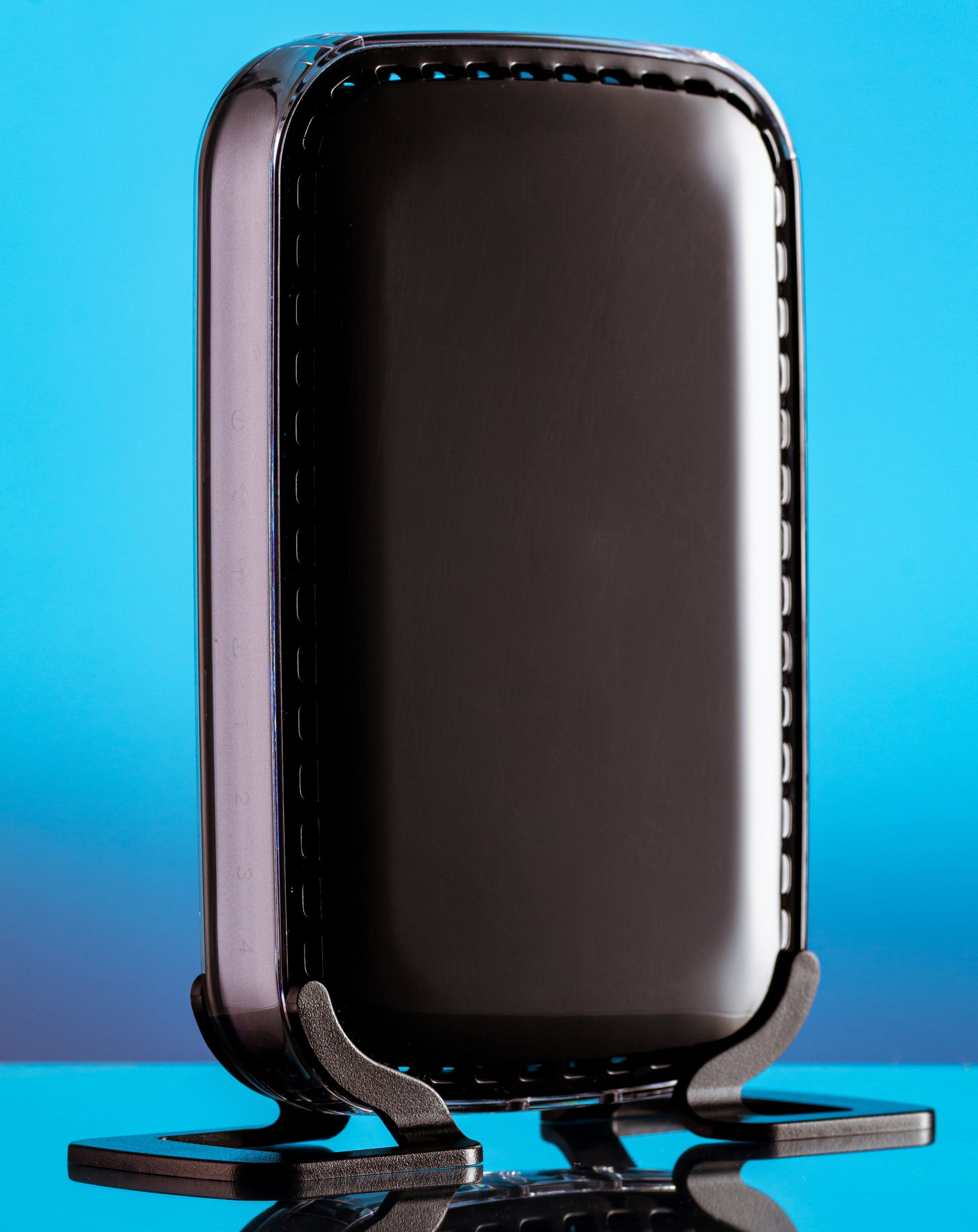 Glossy black rectangular wi-fi router on a reflective surface against a blue background