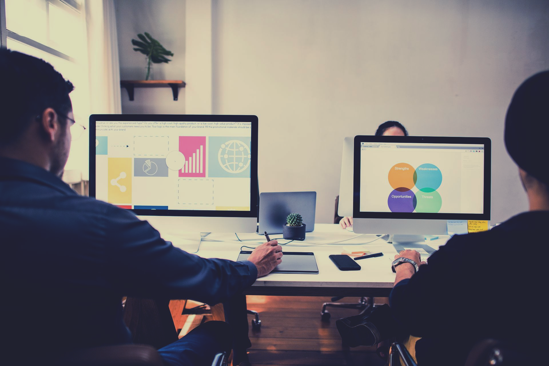 Two people at a desk viewing presentations on dual monitors in a modern office