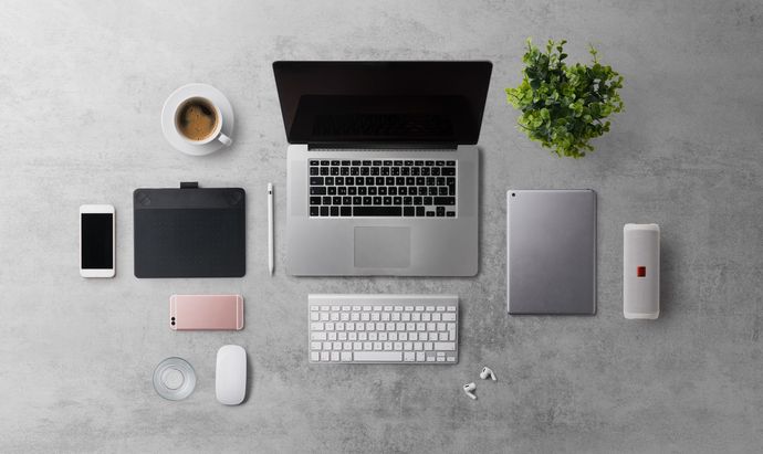 Overhead view of a laptop workspace with keyboard, phone, tablet, coffee, plant, and mouse on a gray desk