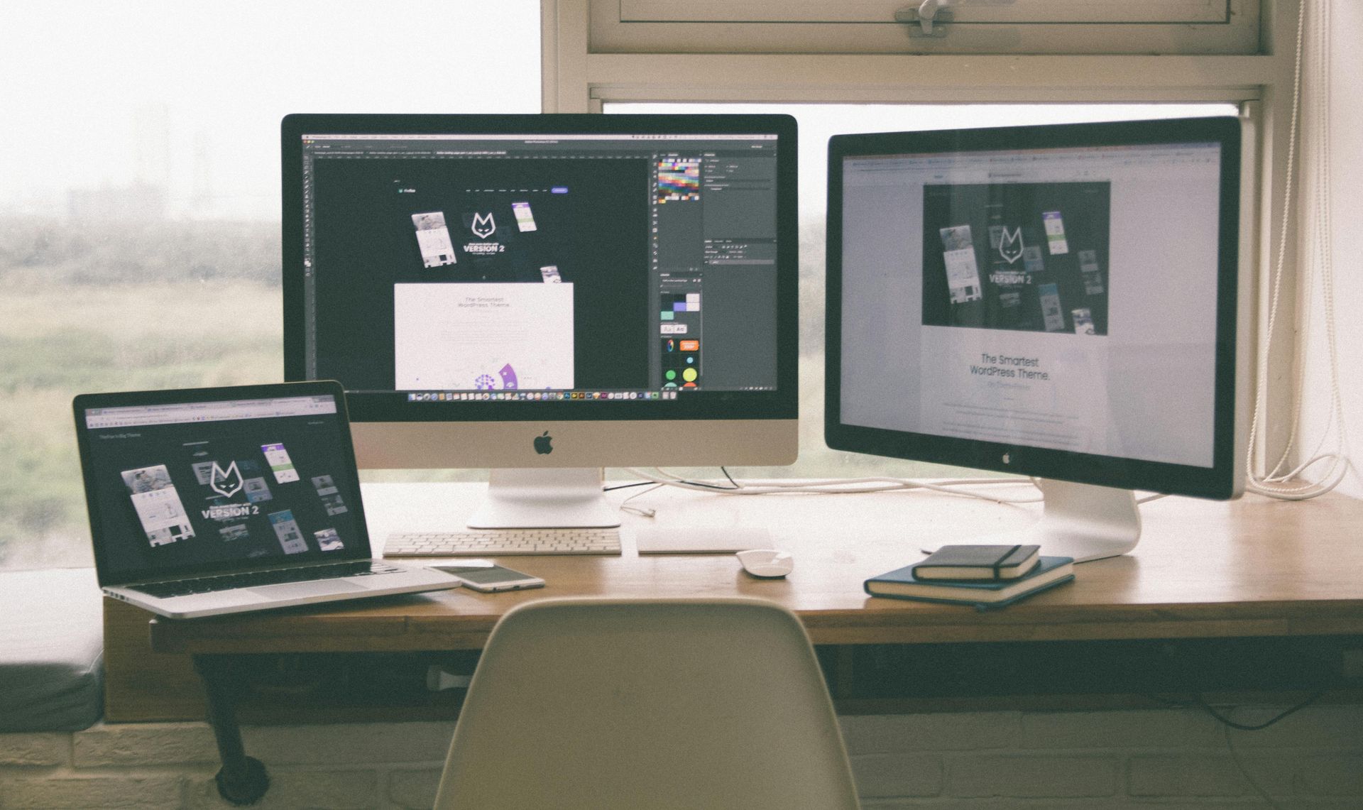 Desk with three screens showing design mockups in a bright workspace.