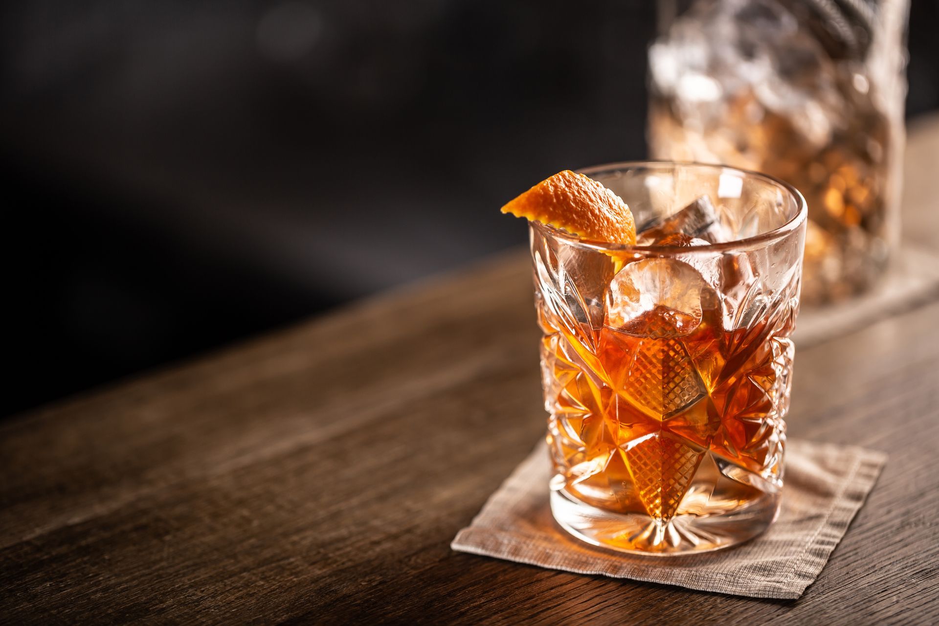 A Glass of Whiskey with Ice and An Orange Peel on A Napkin on A Wooden Table - Lee’s Summit, MO - Top Shelf Bartending Services, LLC