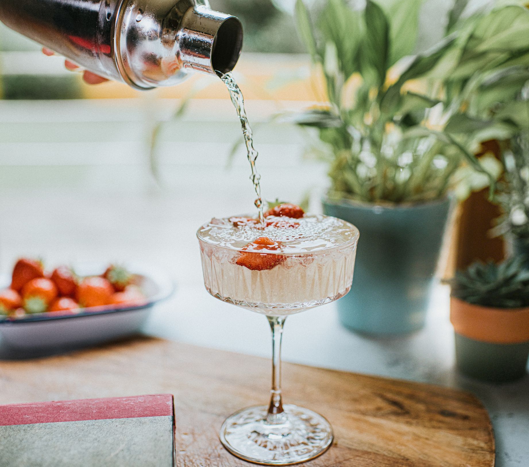 A Person Is Pouring a Drink Into a Wine Glass with Strawberries on Top - Lee’s Summit, MO - Top Shelf Bartending Services, LLC