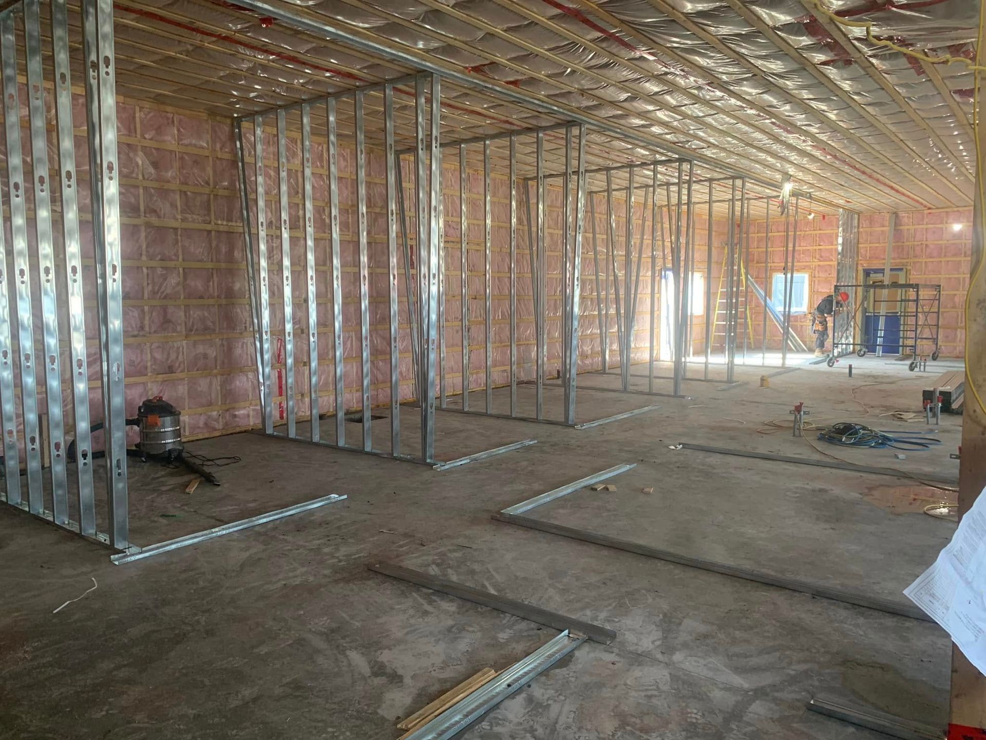 Un chantier de construction intérieur avec une ossature métallique et de l'isolant rose installé sur les murs et le plafond.
