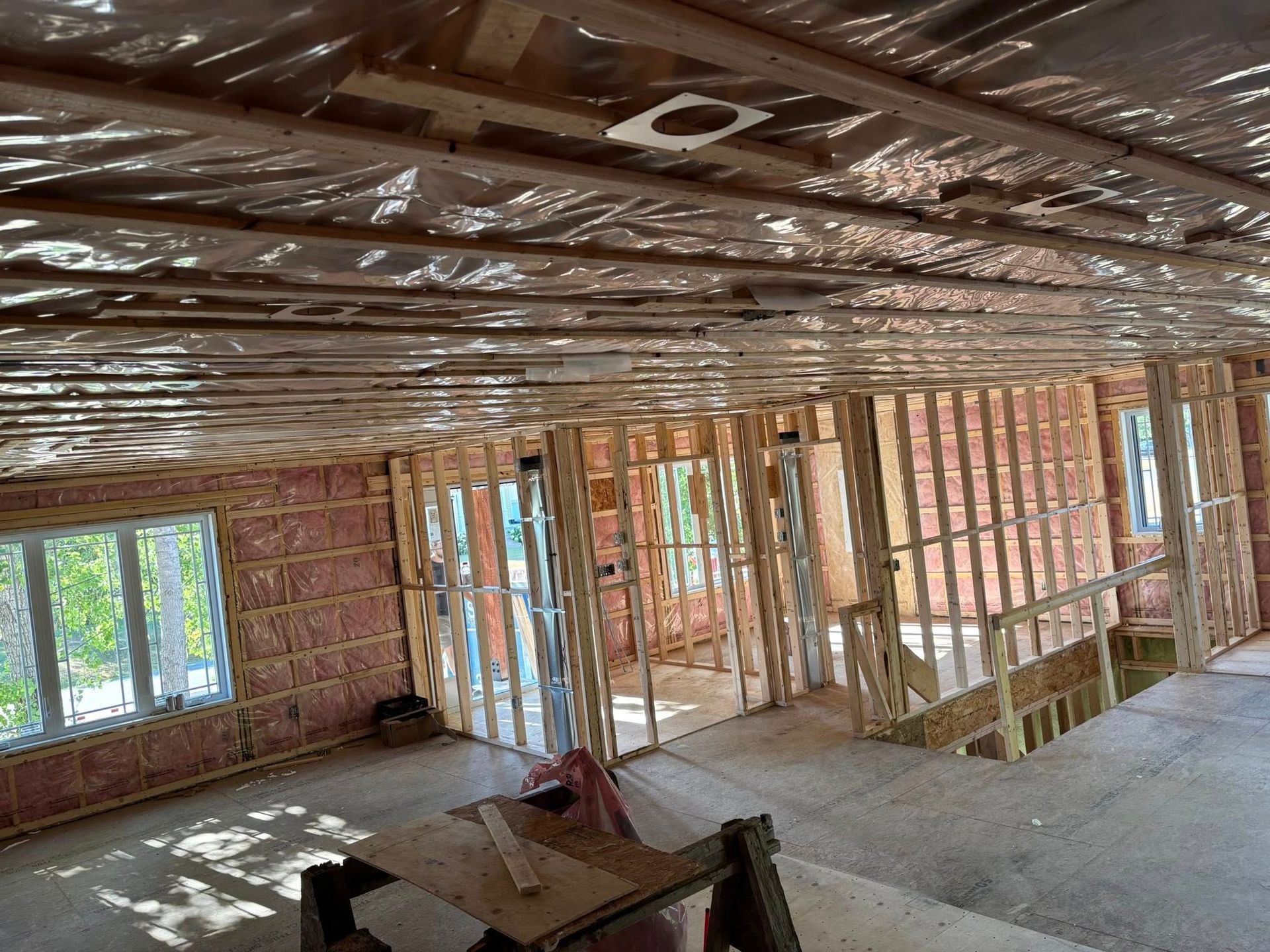 Intérieur d'une maison en construction, montrant des murs à ossature bois, une isolation murale rose et un plafond en tôle plastique.