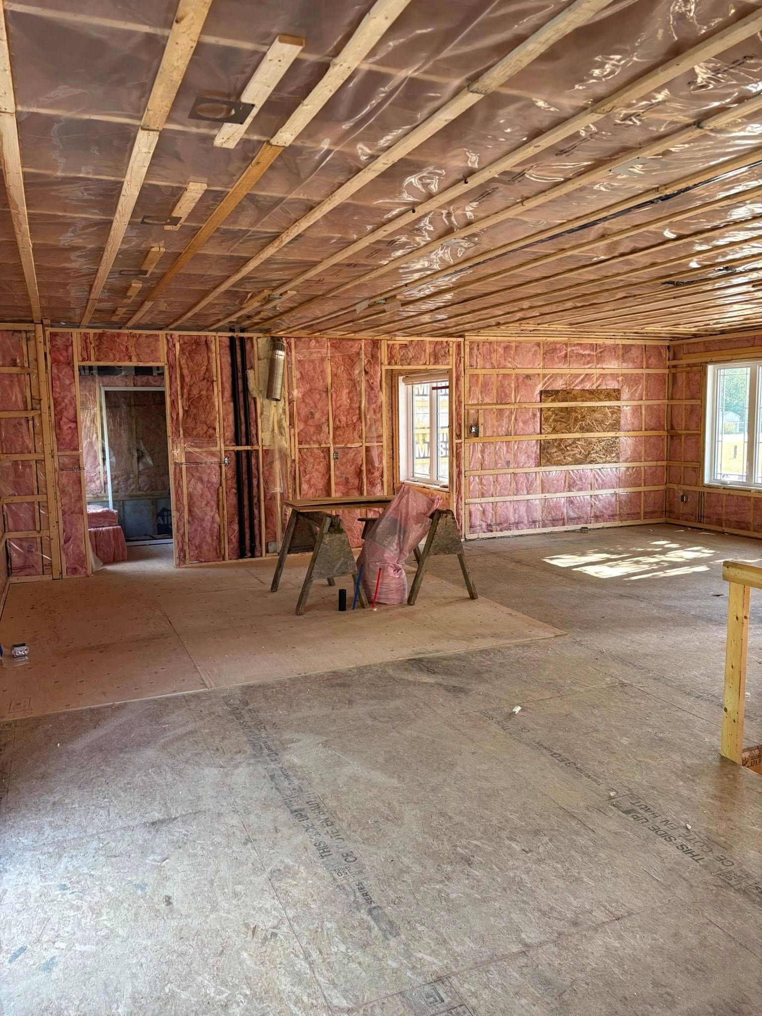 Une pièce en construction avec une isolation en fibre de verre rose dans les murs et un pare-vapeur en plastique au plafond.