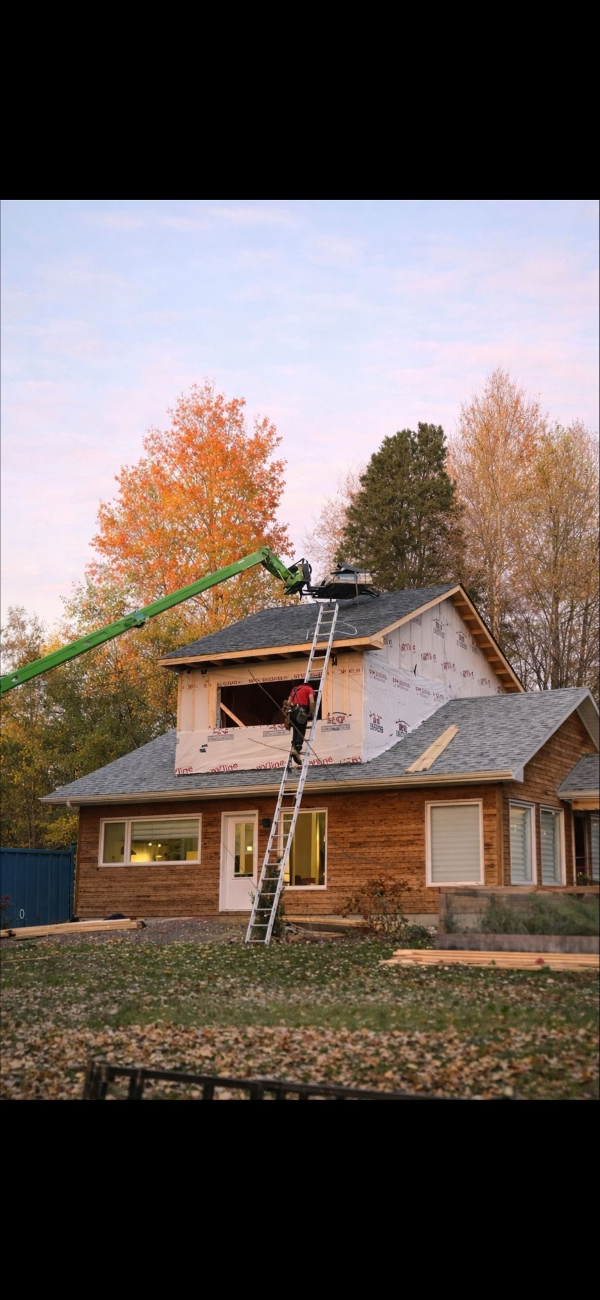 Une personne sur une grande échelle et une autre sur une plateforme de travail surélevée effectuent des travaux de construction sur l'extérieur d'une maison.