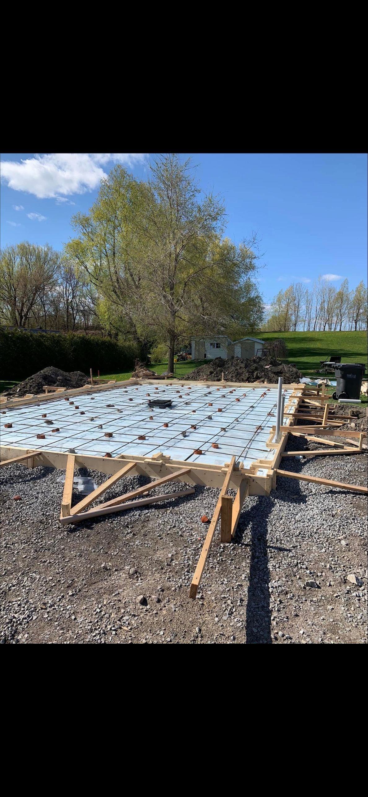 Une dalle de fondation en béton en construction, isolée avec de la mousse bleue, encadrée par des planches de bois sur un sol en gravier.