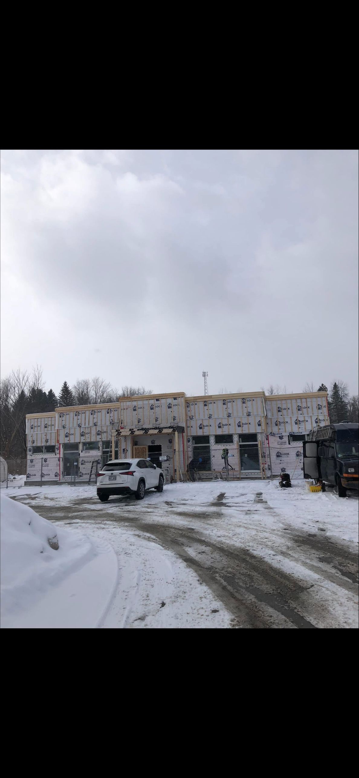 Un bâtiment en construction, aux panneaux d'isolation apparents, se dresse au milieu d'un champ enneigé, une voiture garée devant.