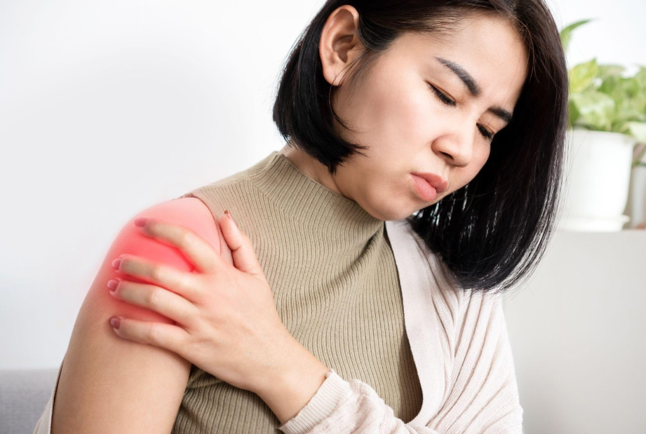 Woman with short black hair holding her right shoulder, showing pain. Red highlighted area indicating injury.
