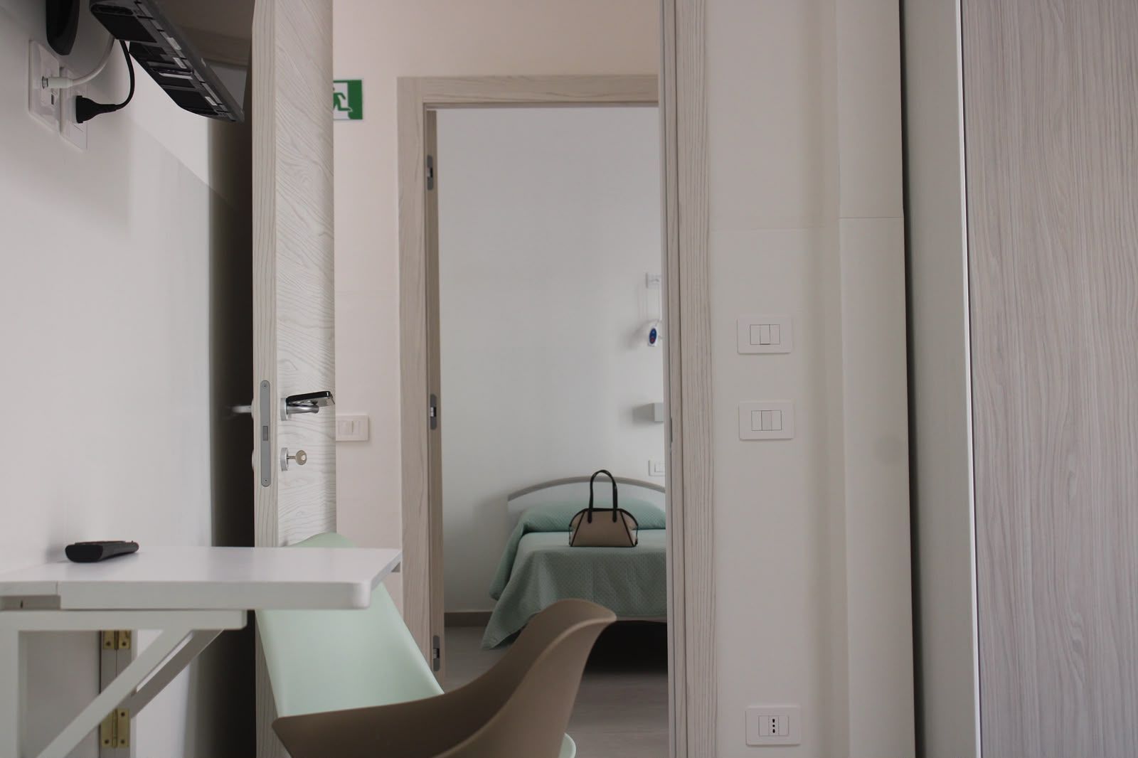 Corridoio luminoso con una porta aperta che dà su una camera da letto con un copriletto color verde acqua