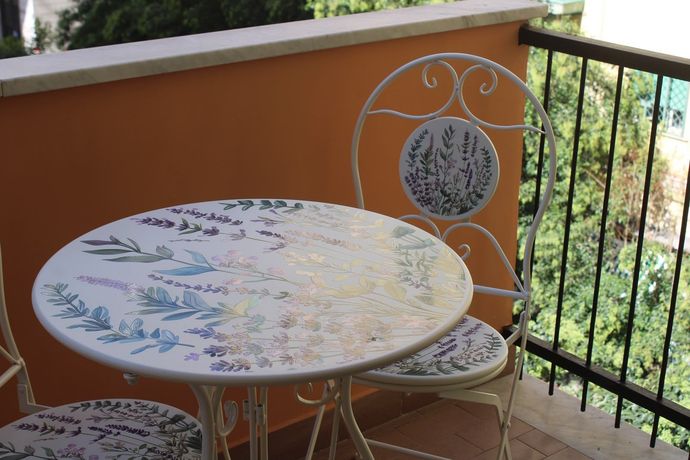 Tavolino rotondo a mosaico e due sedie di metallo su un balcone con pareti arancioni e ringhiera nera