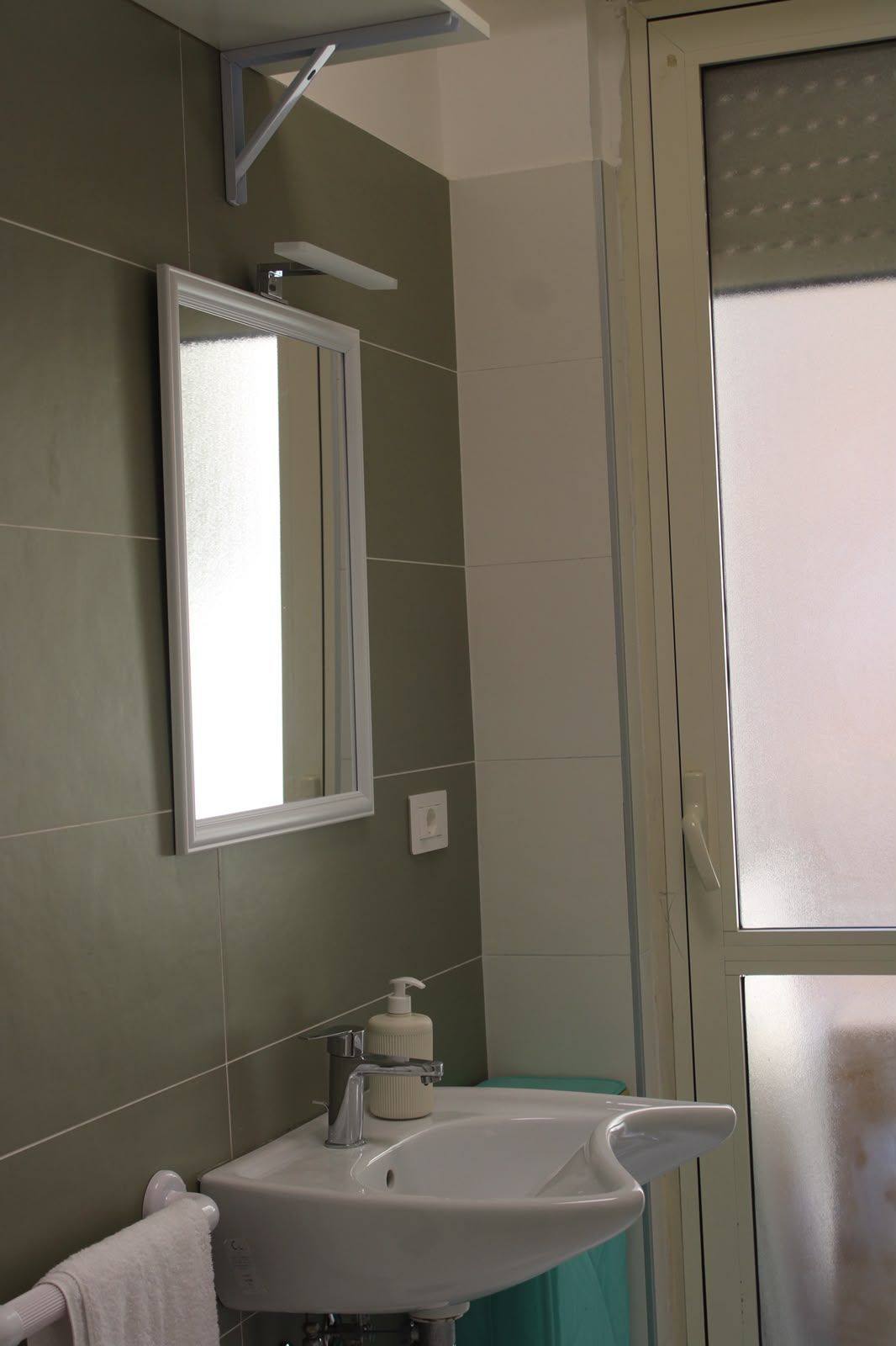 Bagno piccolo con lavabo, specchiera, pareti piastrellate e finestra opaca accanto alla cabina doccia.