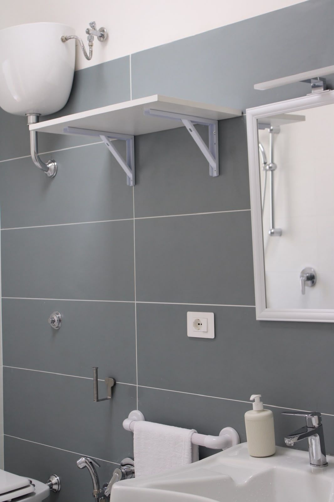 Bagno moderno con parete piastrellata grigia, lavabo, armadietto a specchio, mensola e dispenser di carta igienica a parete