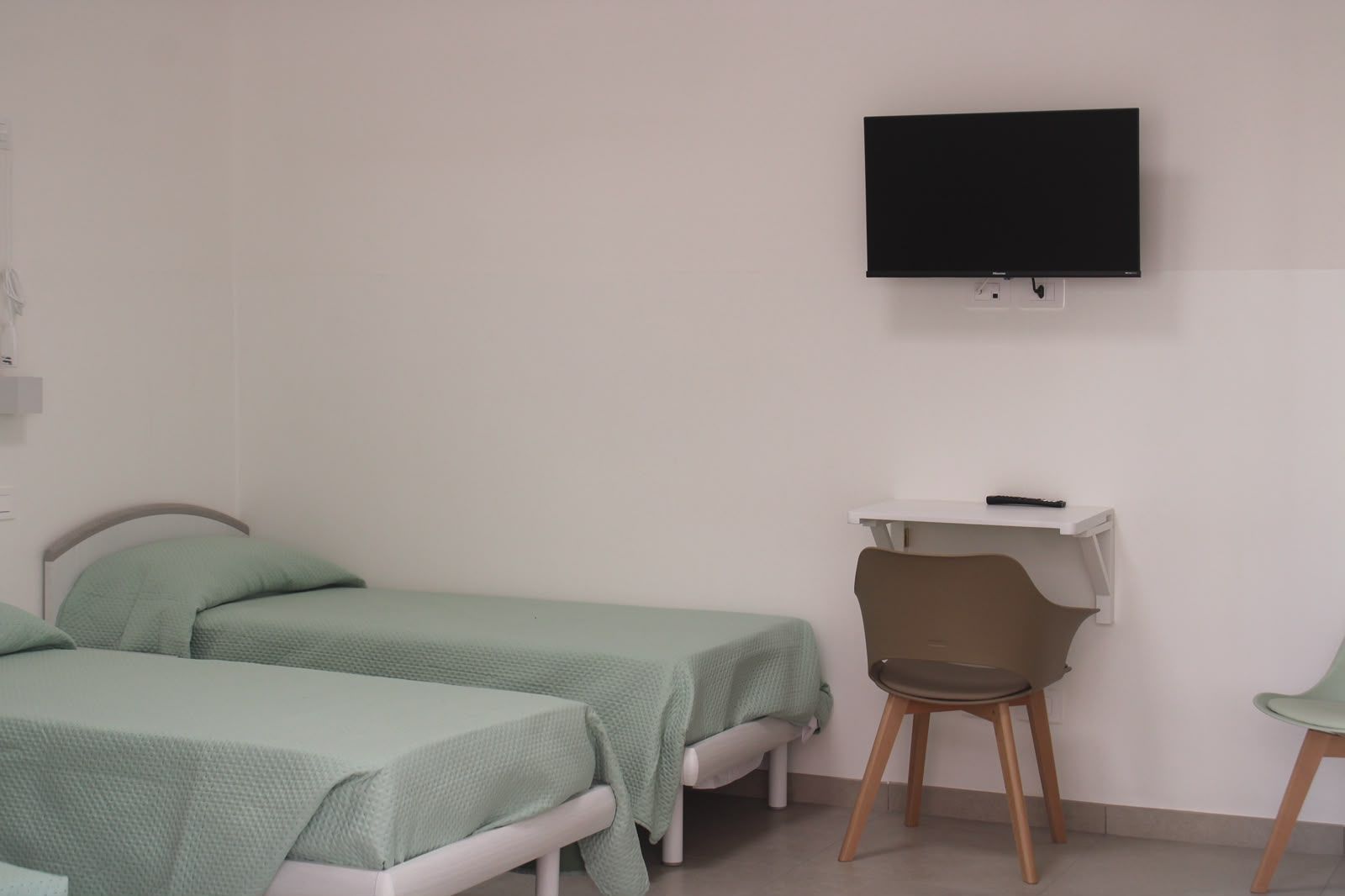Camera semplice con due letti verde menta, una scrivania e una TV a parete