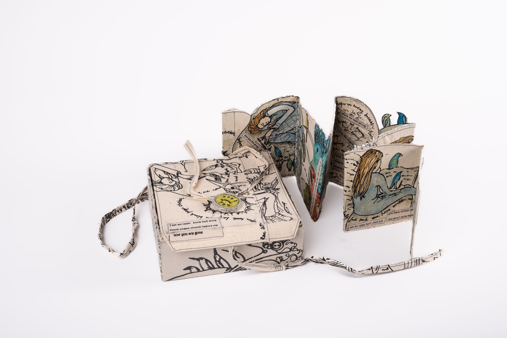 Accordion-style art book open, displaying illustrations. Closed, it's tan with black sketches,