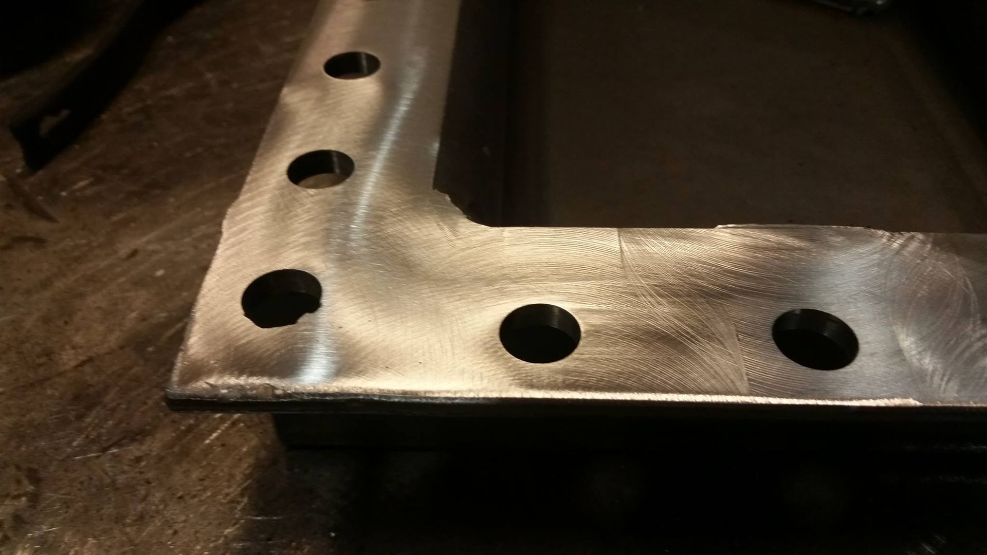 Close-up of a shiny metal L-bracket with evenly spaced circular holes.