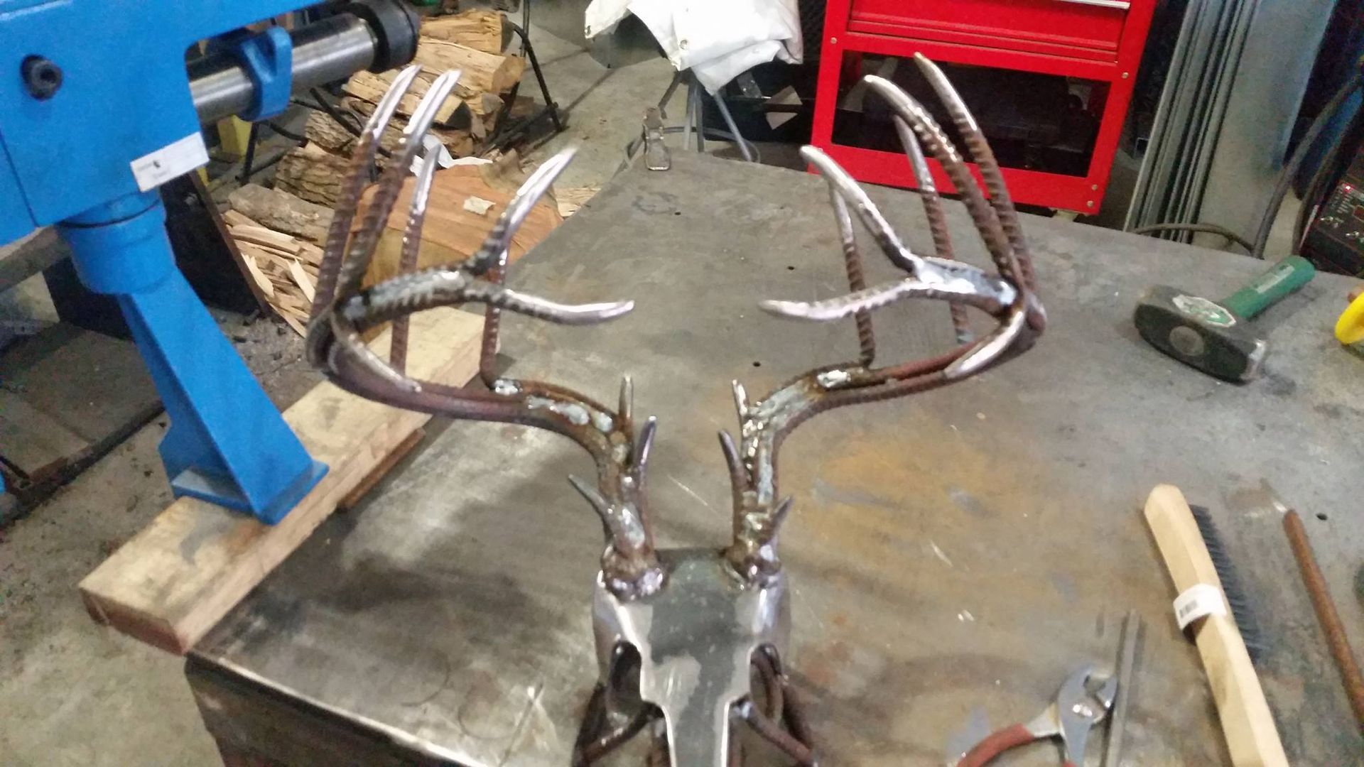 Metal antler-shaped sculpture on a workbench in a workshop, with tools and equipment nearby