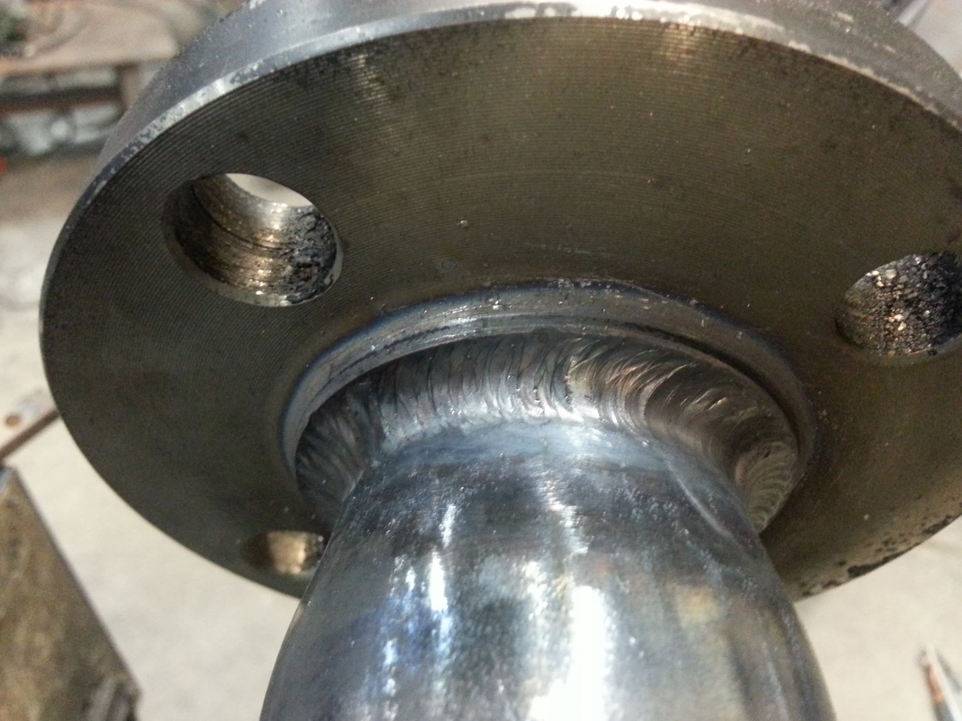 Close-up of a metal pipe welded into a circular flange with bolt holes