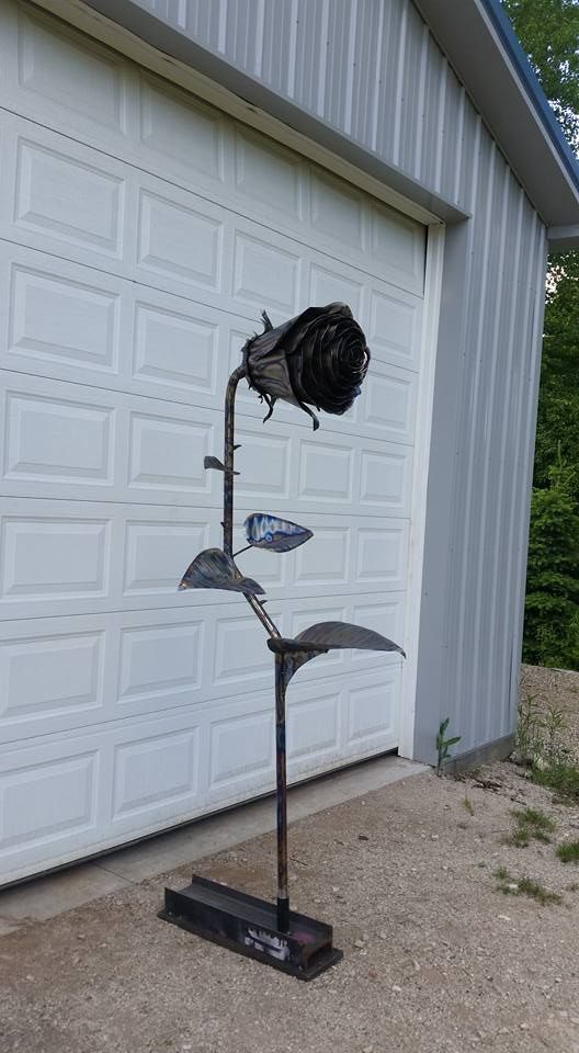 Black metal flower sculpture on a base, standing in front of a white garage door outdoors