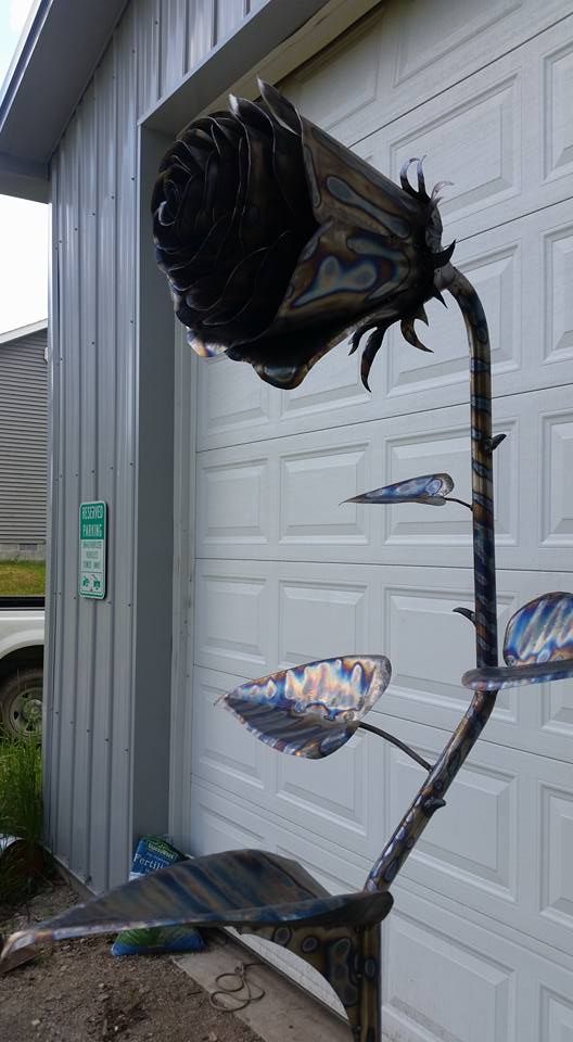 Metal sculpture with dark bird-like top and colorful branch-like elements beside a garage door