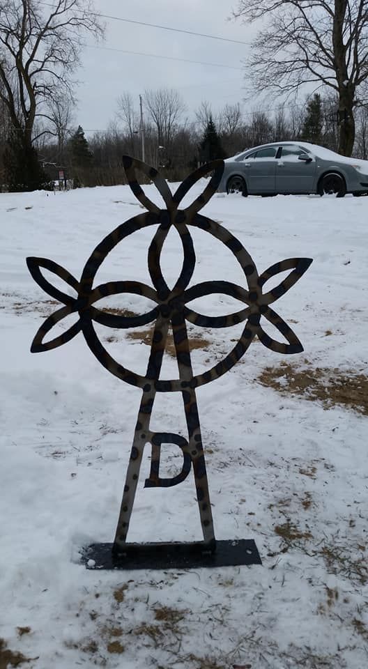 Black metal decorative sculpture in a snowy yard, with bare trees and a parked car in the background