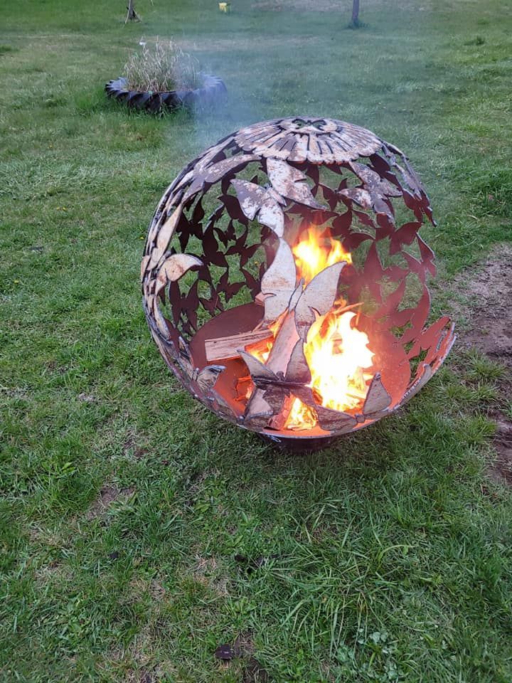 Metal fire pit burning on a grassy lawn, with another fire pit in the background.