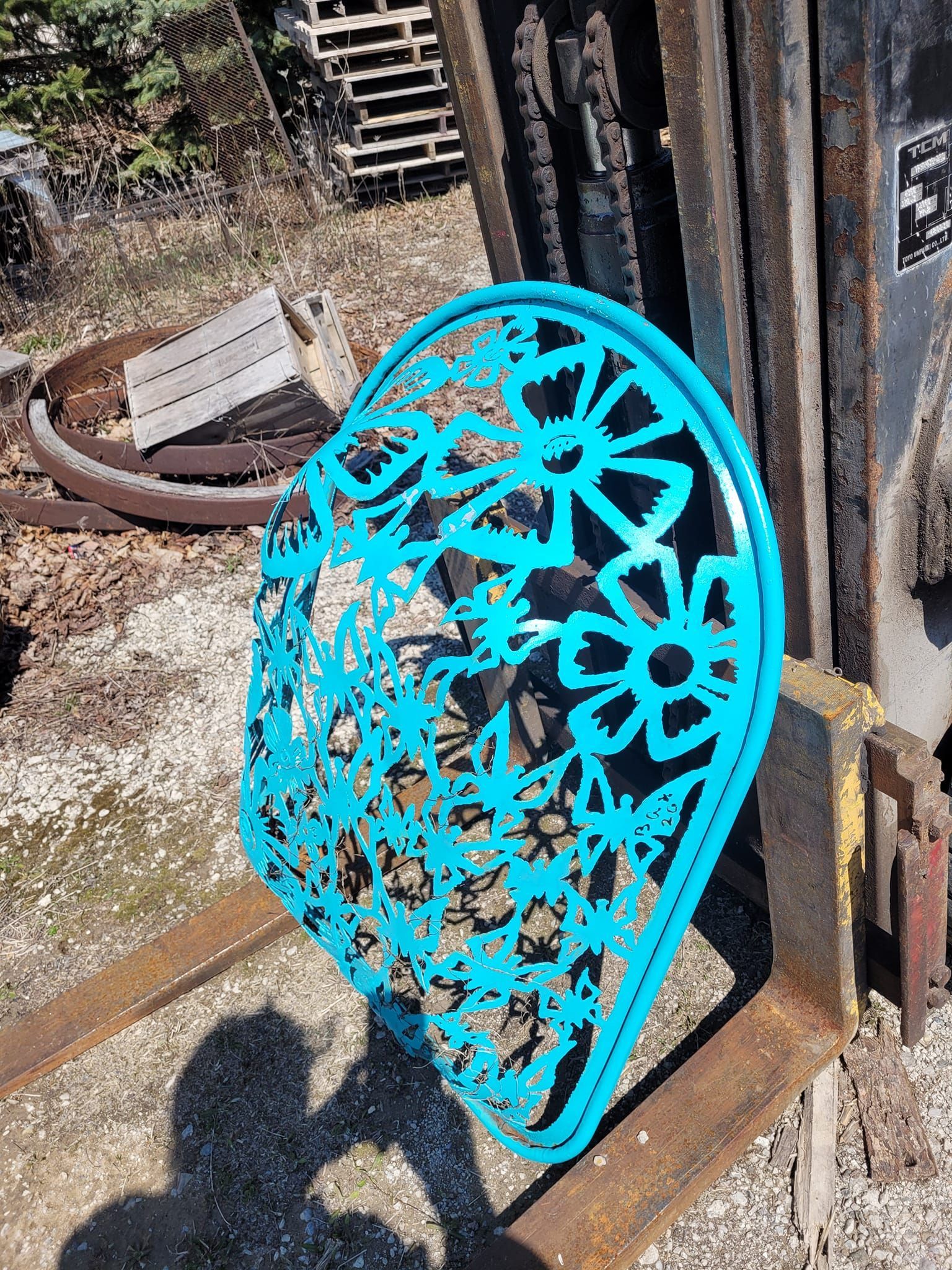 Bright turquoise metal floral wall decoration leaning against a rusty post outdoors.
