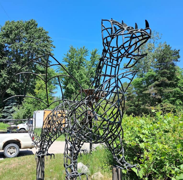 Metal horse sculpture in a grassy field with trees and blue sky behind it