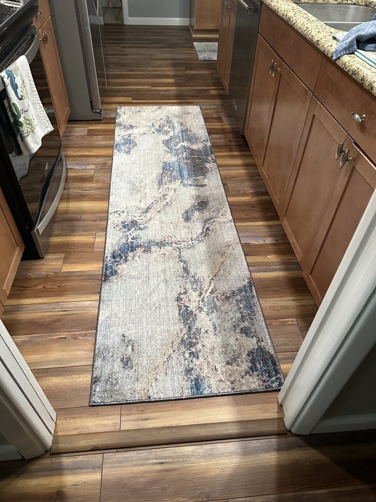 A kitchen with hardwood floors and a rug on the floor.