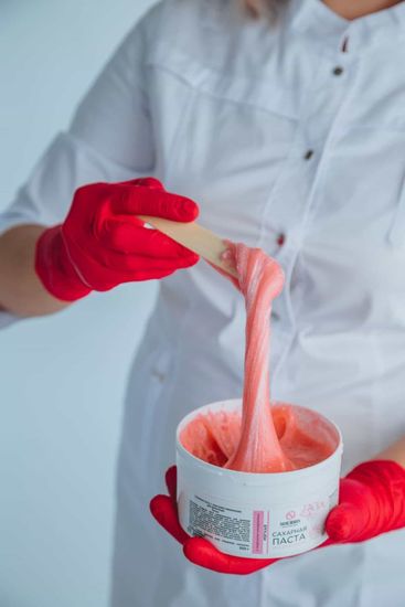 Person in white coat and red gloves lifting pink wax from a container