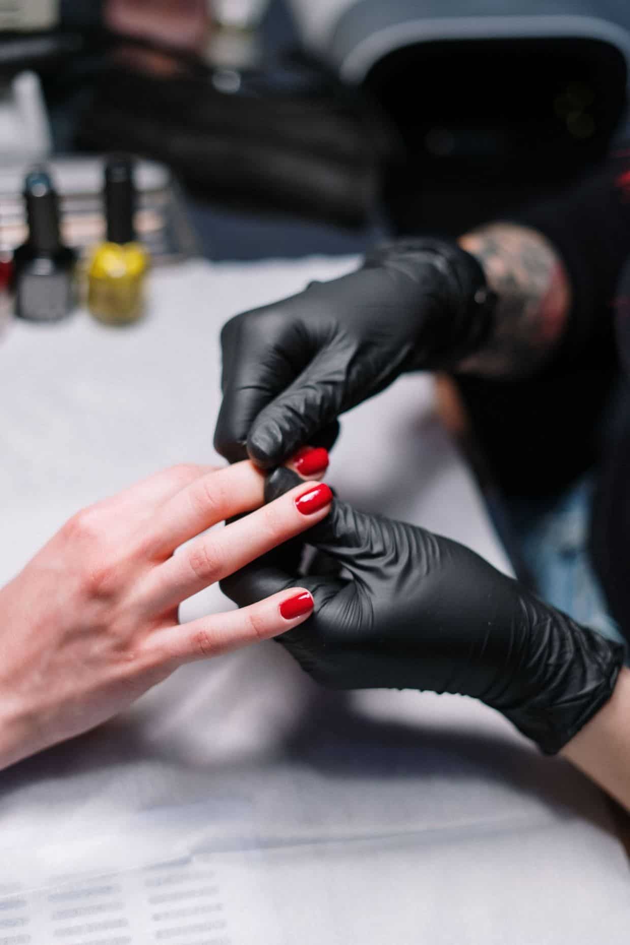 Black-gloved manicurist painting red nails on a client's hand