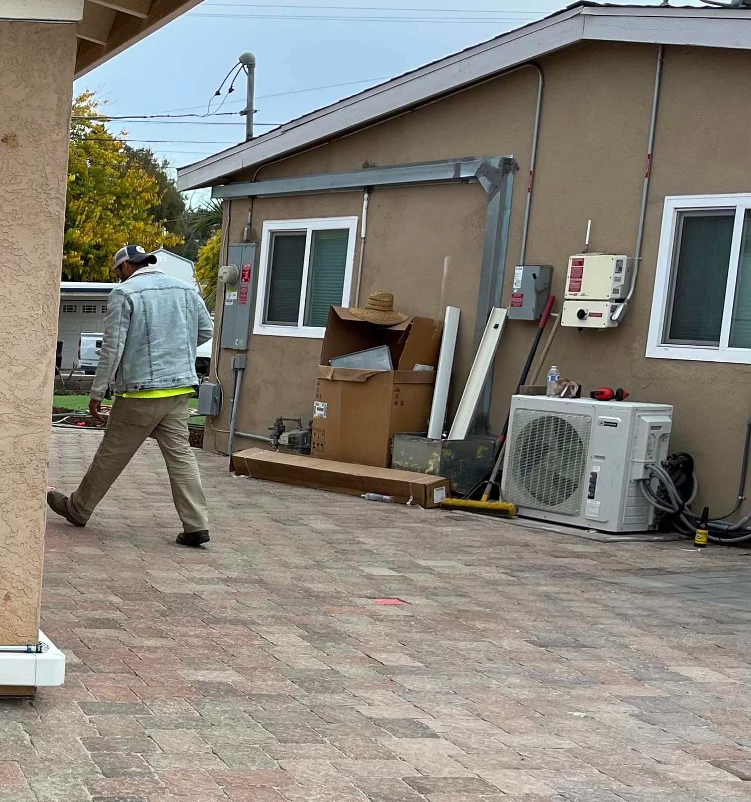 A man is walking on a brick sidewalk in front of a house.