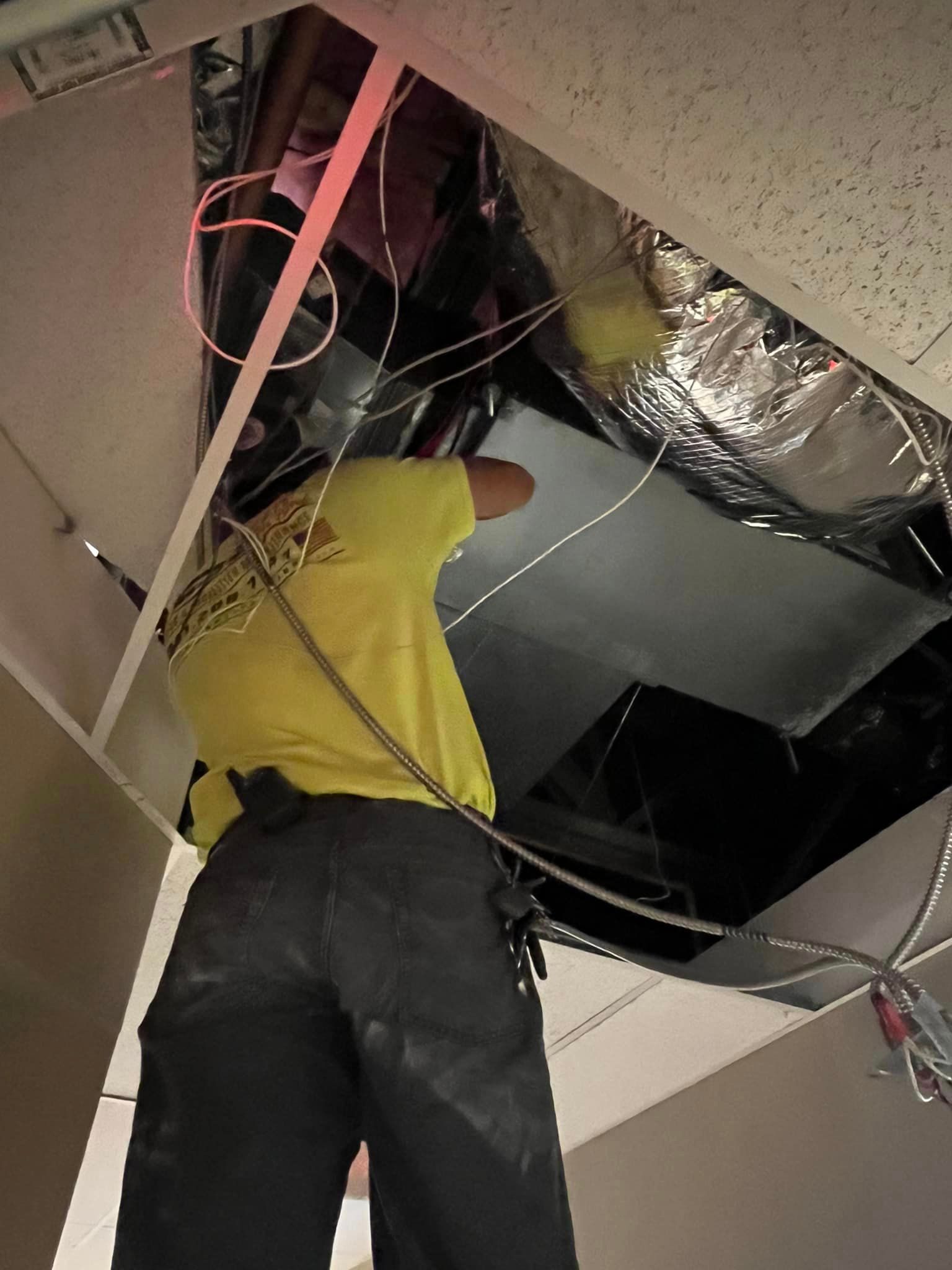 A man in a yellow shirt is working on a ceiling.