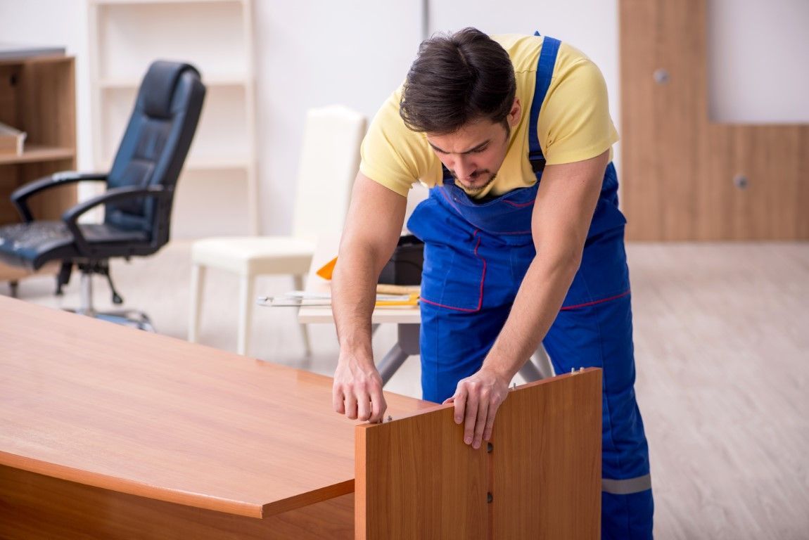 Worker in blue overalls assembling a wooden desk in an office room