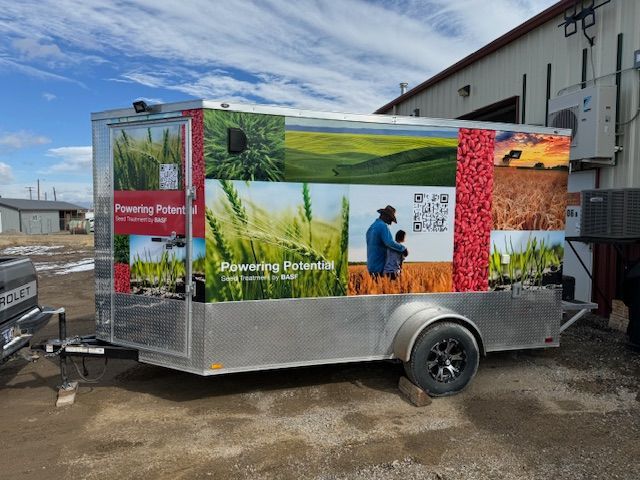 A trailer with a colorful agricultural advertisement. Photos of wheat fields, farmers, and QR codes adorn the sides.