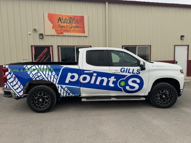 White pickup truck with blue Point S tire shop logo, parked outside the shop.