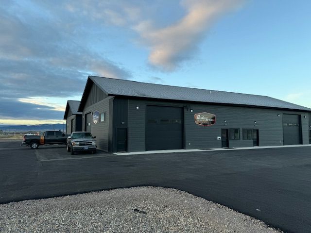 Dark gray building with large garage doors, parked cars, and cloudy sky.