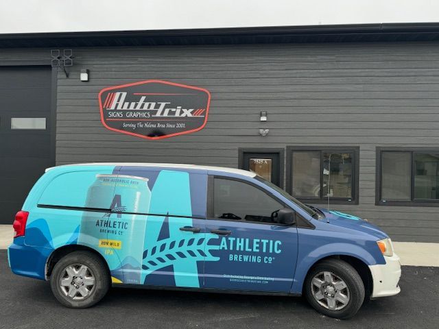 Blue van with Athletic Brewing Co. graphics parked in front of a building with a logo that says 