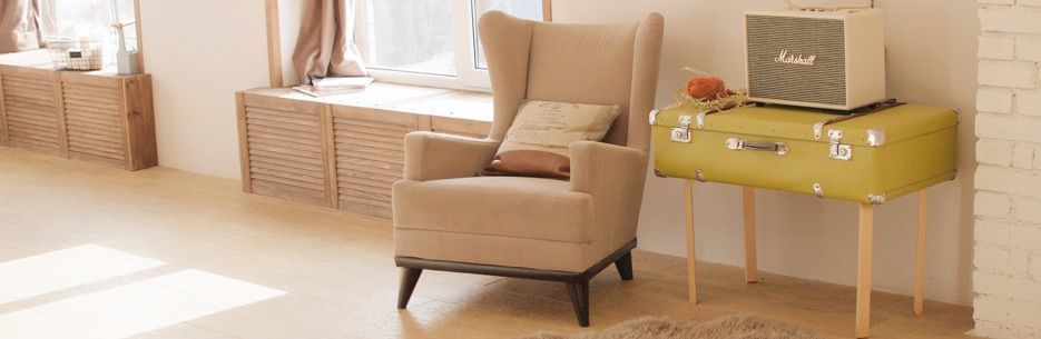 A cozy living room with a beige armchair, a yellow suitcase table, and a Marshall speaker.