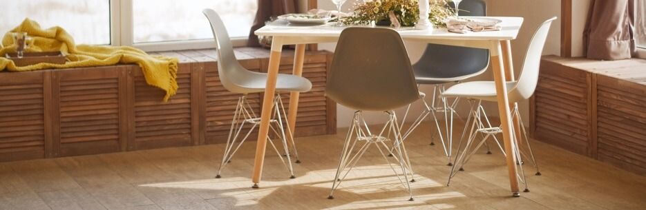 Dining table with white top and wooden legs; four chairs with wooden legs and colored plastic seats; window seat.