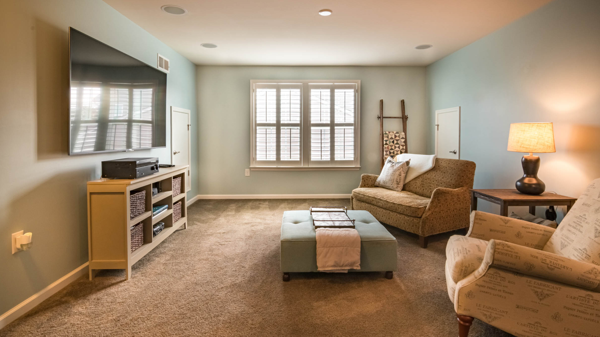 Living room with TV, seating, and window; pale blue walls, neutral carpet.
