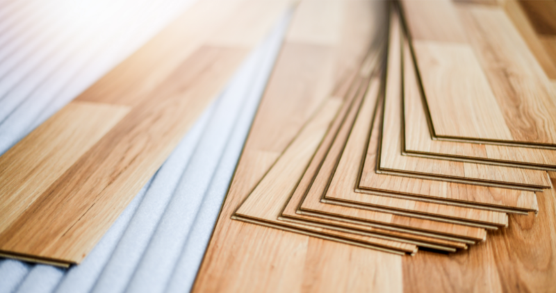 Multiple light-wood laminate or timber flooring planks stacked diagonally, displaying their grooves.