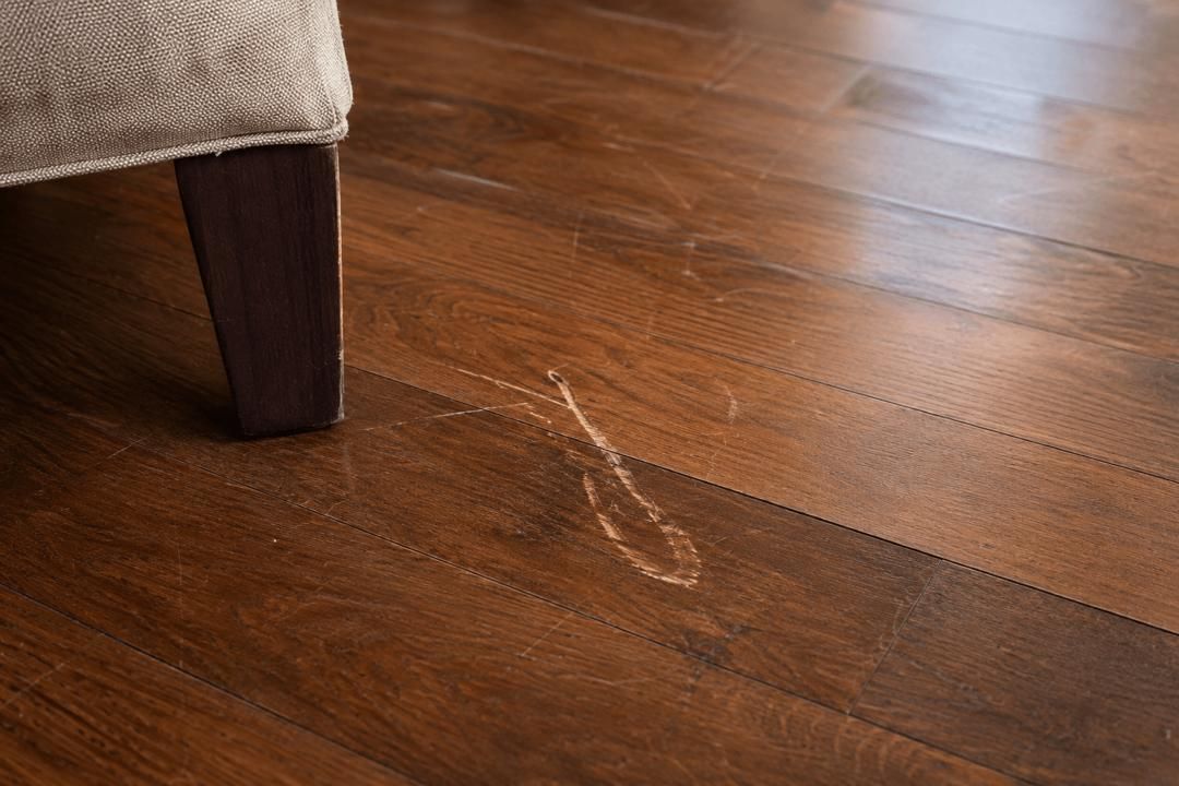 Wooden floor with a faint heart-shaped water stain beside a furniture leg