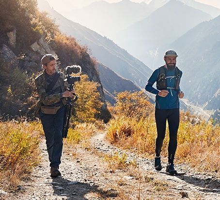 Two men are walking down a dirt path with mountains in the background