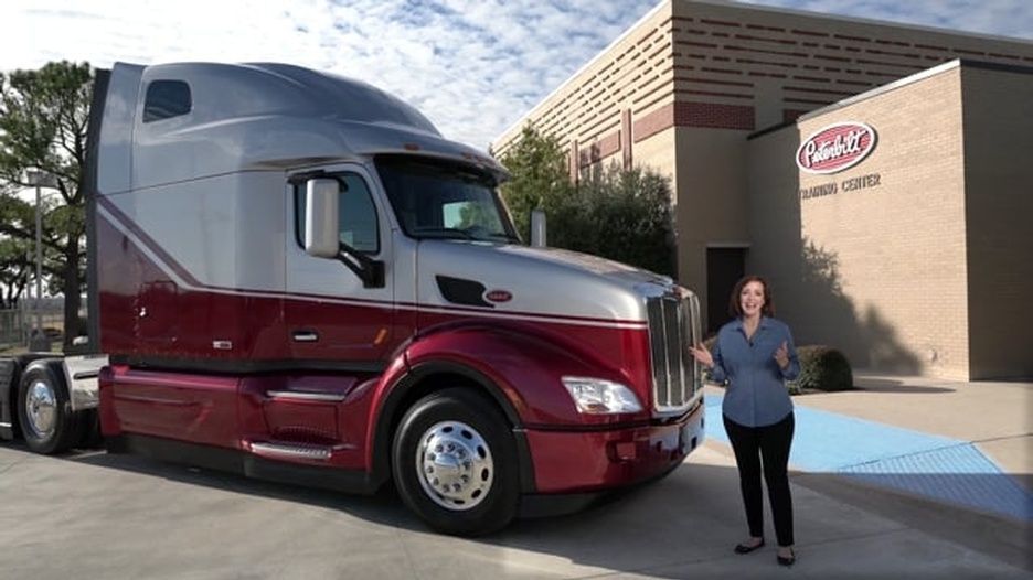 A woman is standing in front of a large semi truck
