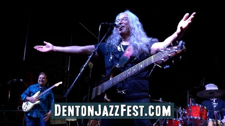 A man with long hair is playing a guitar and singing into a microphone on a stage