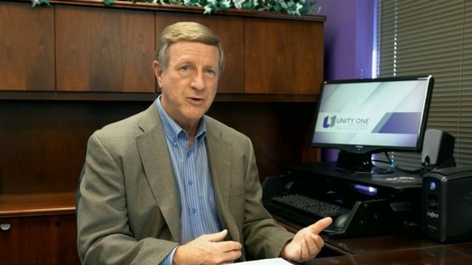 A man in a suit is sitting at a desk in front of a computer
