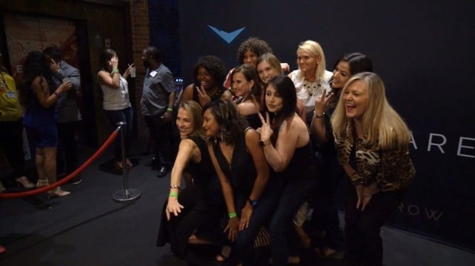 A group of women are posing for a picture in front of a black wall