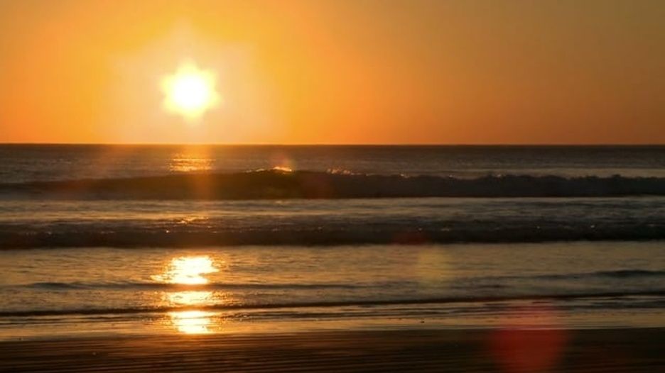 The sun is setting over the ocean and the waves are crashing on the beach